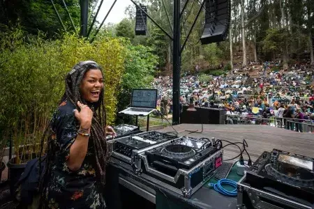 A woman DJing at the Stern Grove Festival looks over her shoulder and smiles into the camera.